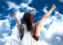 Girl raising her arms to clouds victoriously.