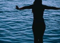 Silhouette of girl standing over water.