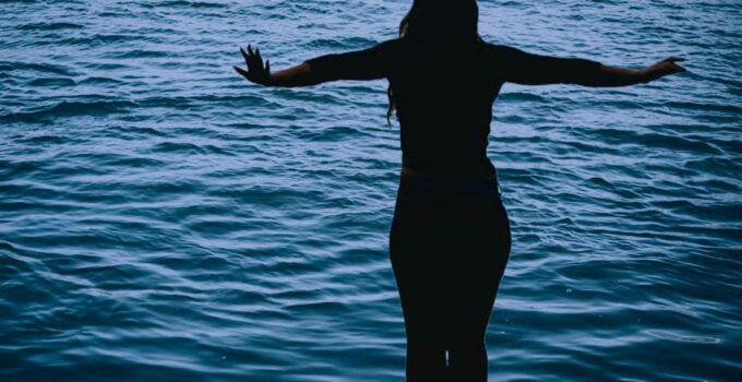 Silhouette of girl standing over water.
