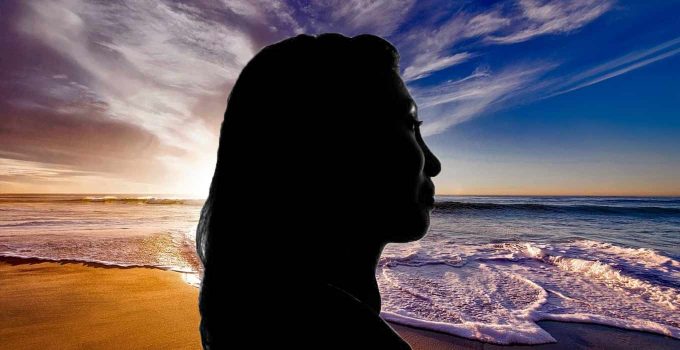 Silhouette of woman meditating before ocean